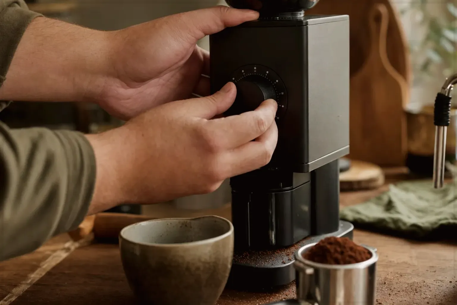 Zwei Hände stellen den Mahlgrad an einer Kaffeemühle neben einer Espressomaschine ein – gezeigt für Marken in der Herstellerübersicht im Orientierungsbereich.