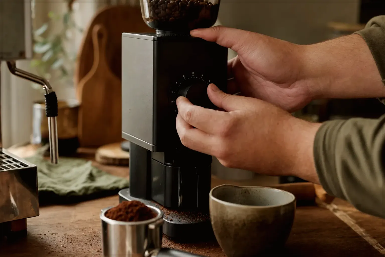Zwei Hände stellen den Mahlgrad an einer Kaffeemühle neben einer Espressomaschine ein – gezeigt für Kaffeemaschinen im Themenvergleich.