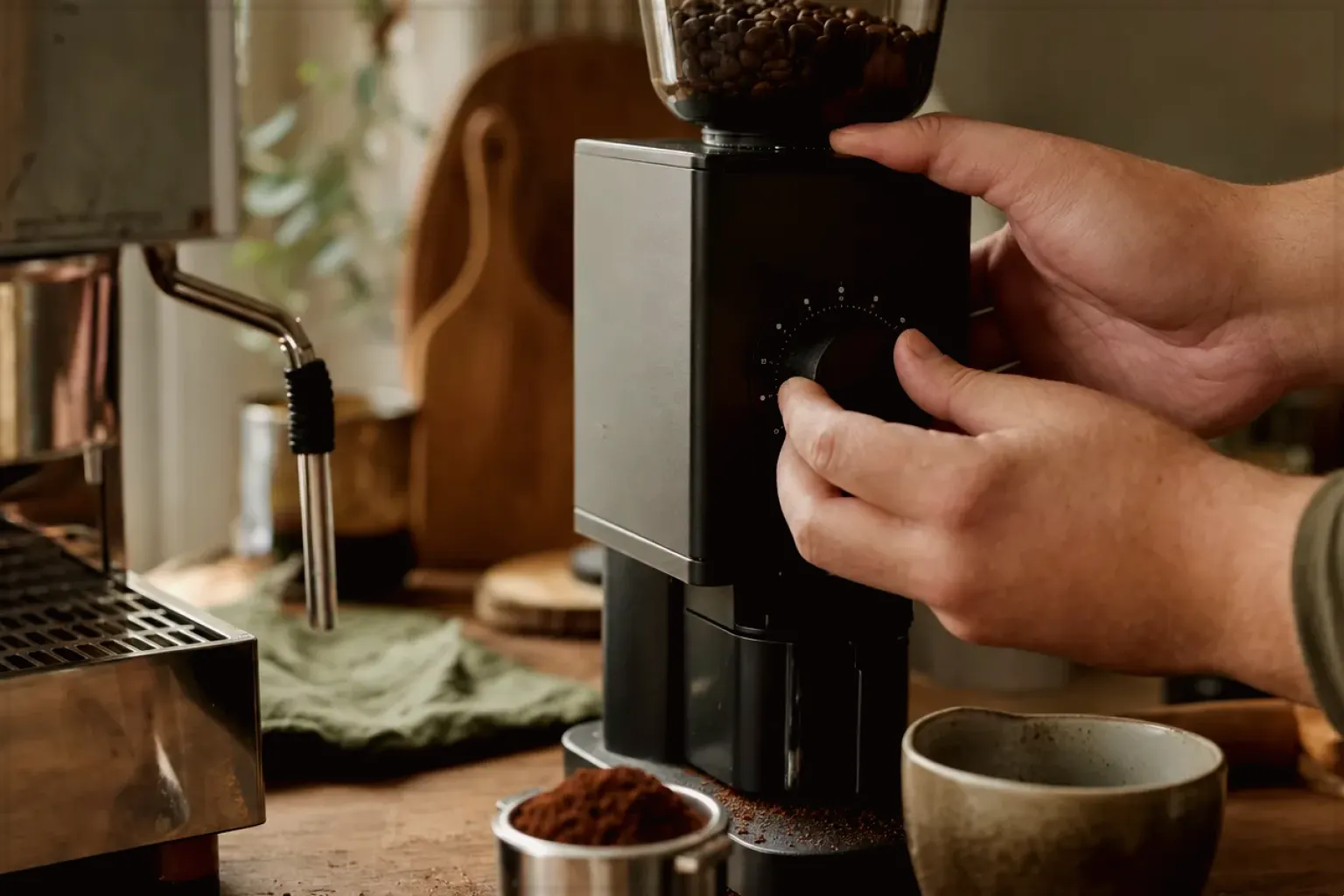 Zwei Hände stellen den Mahlgrad an einer Kaffeemühle neben einer Espressomaschine ein – gezeigt für Siebträger für Einsteiger im Themenvergleich.