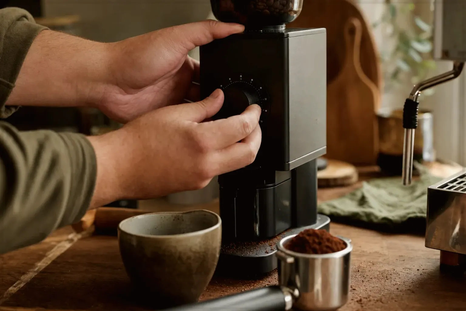 Zwei Hände stellen den Mahlgrad an einer Kaffeemühle neben einer Espressomaschine ein – gezeigt für Comandante C40 MK4 im Produktprofil.
