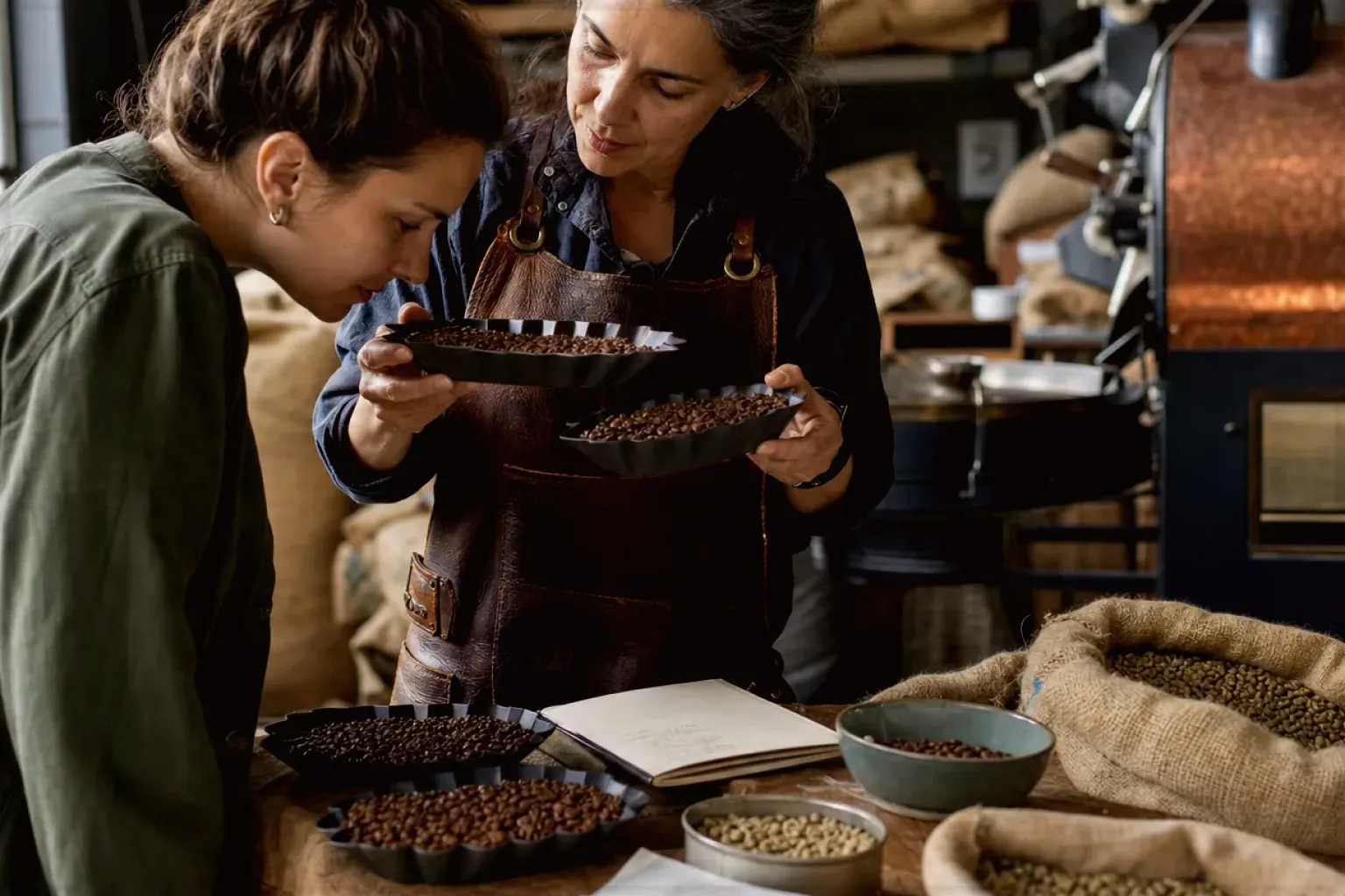 Eine Kaffeerösterin lässt eine Kundin in einer kleinen Rösterei verschiedene frisch geröstete Bohnen riechen – gezeigt für Melitta AromaFresh II Therm im Produktprofil.