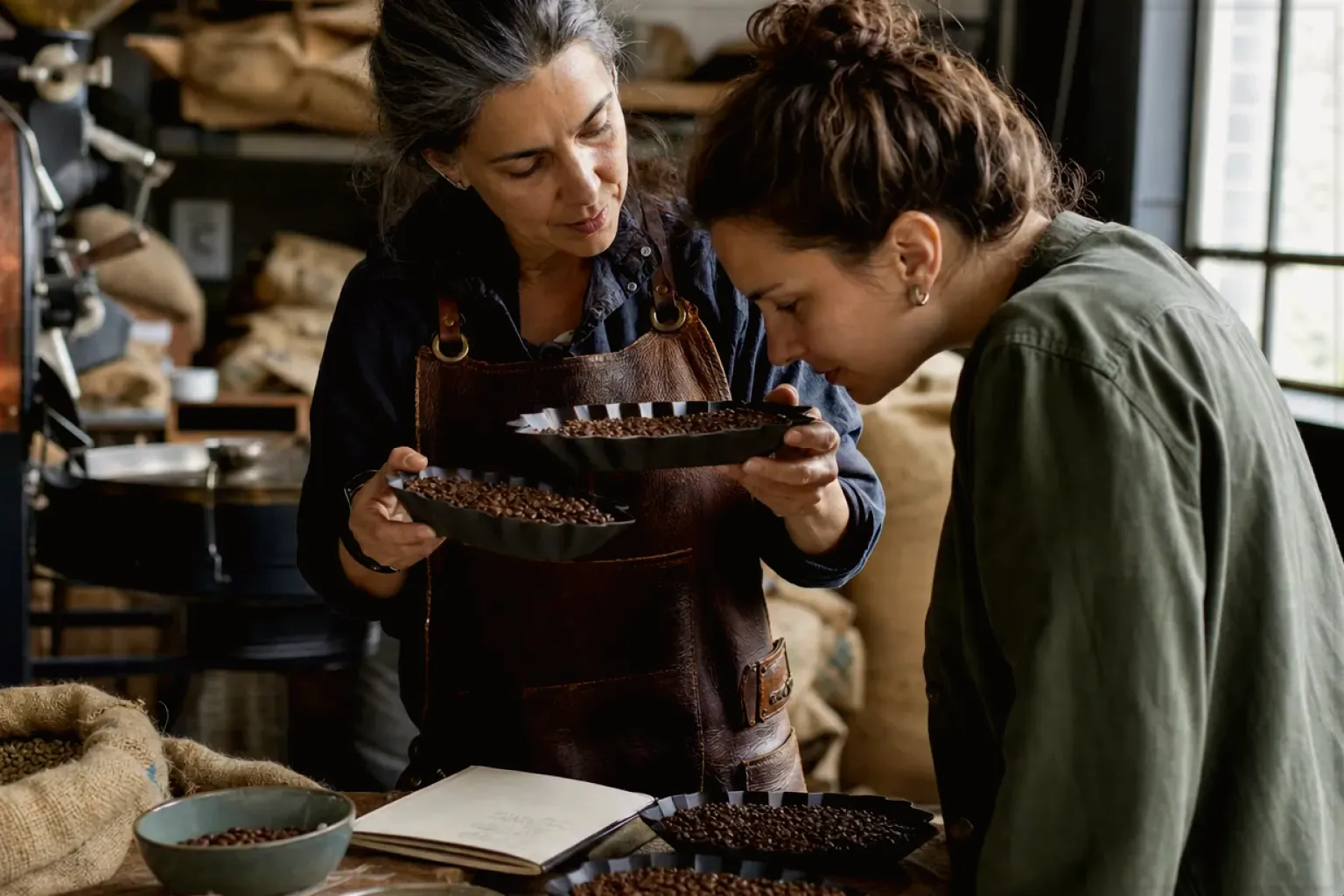 Eine Kaffeerösterin lässt eine Kundin in einer kleinen Rösterei verschiedene frisch geröstete Bohnen riechen – gezeigt für Sage Barista Express Impress im Produktprofil.