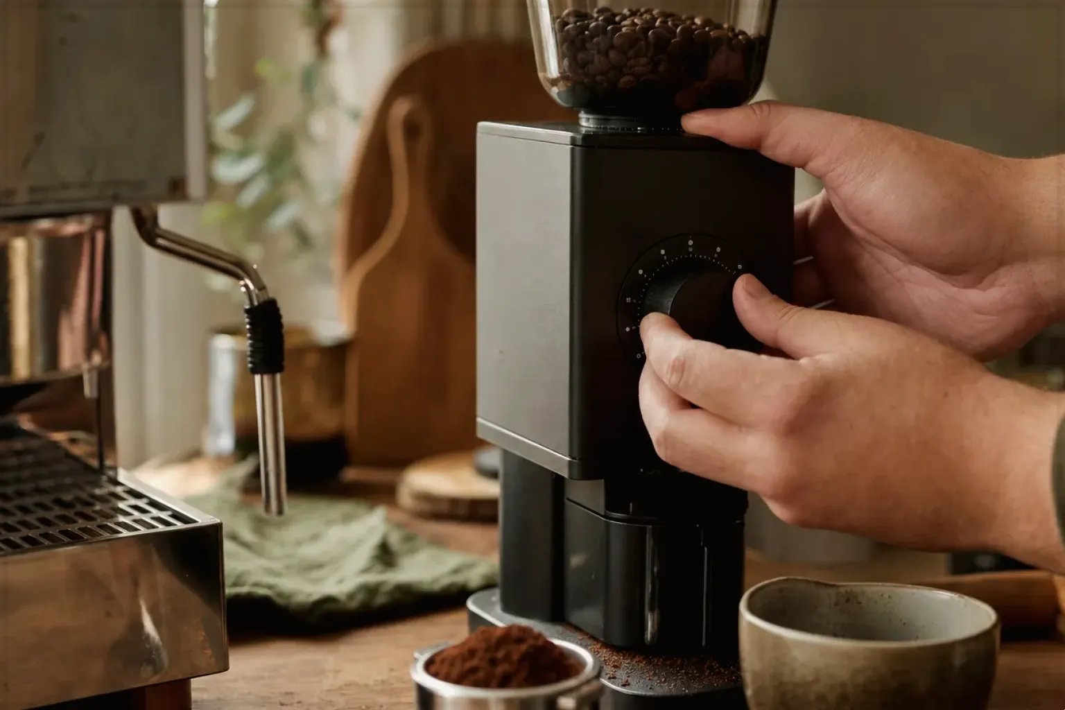 Zwei Hände stellen den Mahlgrad an einer Kaffeemühle neben einer Espressomaschine ein – gezeigt für Vollautomaten-Beratung im Kaufberatung.